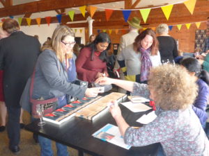 3 people standing around book stall, one paying for a book and the others browsing. People and bunting in background.