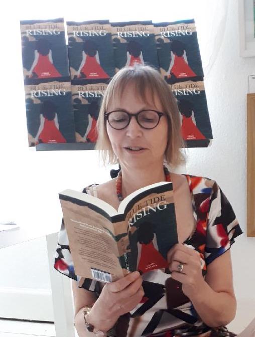 Image of Clare Stevens reading Blue Tide Rising at Butterflies in Nottingham with white wall and artwork behind her